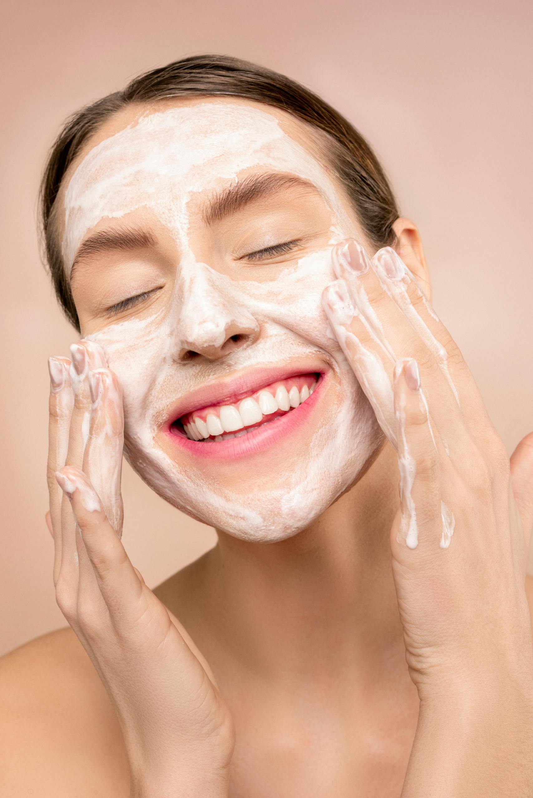 Contact 3 Smiling woman applies facial wash while enjoying her skincare routine, promoting happiness and skin health.